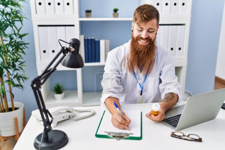 Téléchargez les photos : Jeune rousse homme portant un uniforme de médecin prescrire des pilules à la clinique - en image libre de droit