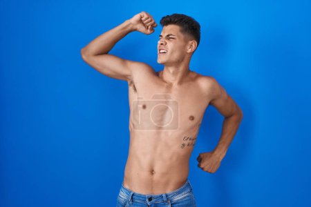 Photo for Young hispanic man standing shirtless over blue background stretching back, tired and relaxed, sleepy and yawning for early morning - Royalty Free Image
