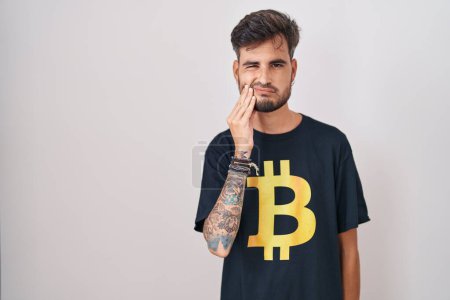 Téléchargez les photos : Young hispanic man with tattoos wearing bitcoin t shirt touching mouth with hand with painful expression because of toothache or dental illness on teeth. dentist concept. - en image libre de droit