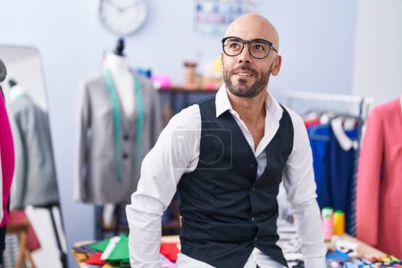 Téléchargez les photos : Jeune tailleur chauve souriant confiant debout au magasin de tailleur - en image libre de droit