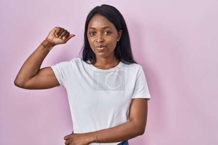 Téléchargez les photos : African young woman wearing casual white t shirt strong person showing arm muscle, confident and proud of power - en image libre de droit
