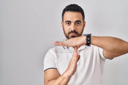 Photo for Young hispanic man with beard wearing casual clothes over white background doing time out gesture with hands, frustrated and serious face - Royalty Free Image