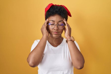 Foto de Young african american woman standing over yellow background with hand on head, headache because stress. suffering migraine. - Imagen libre de derechos