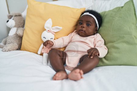 Téléchargez les photos : African american baby sitting on bed with relaxed expression at bedroom - en image libre de droit