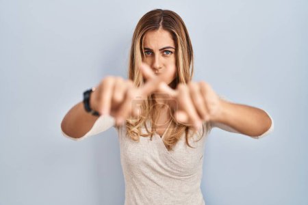Foto de Young blonde woman standing over isolated background rejection expression crossing fingers doing negative sign - Imagen libre de derechos