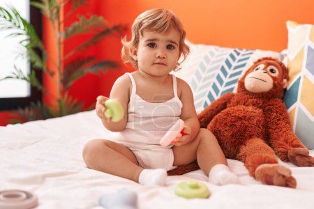 Foto de Adorable niño hispano jugando con juguete sentado en la cama en el dormitorio - Imagen libre de derechos