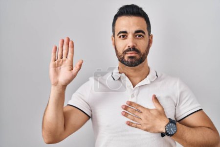 Photo for Young hispanic man with beard wearing casual clothes over white background swearing with hand on chest and open palm, making a loyalty promise oath - Royalty Free Image