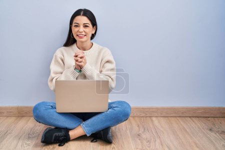 Photo for Young woman using laptop sitting on the floor at home with hands together and crossed fingers smiling relaxed and cheerful. success and optimistic - Royalty Free Image