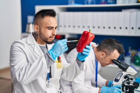 Téléchargez les photos : Two men scientist injecting liquid on red pepper using microscope at laboratory - en image libre de droit