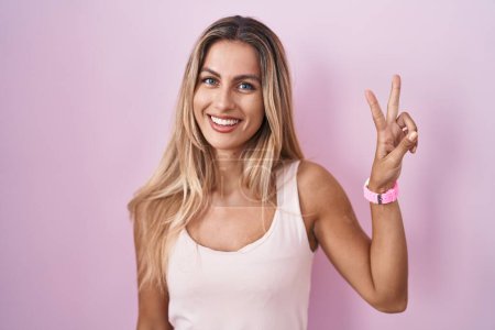 Téléchargez les photos : Jeune femme blonde debout sur fond rose montrant et pointant vers le haut avec les doigts numéro deux tout en souriant confiant et heureux. - en image libre de droit