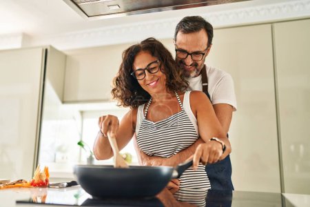 Téléchargez les photos : Moyen âge couple hispanique souriant confiant et se serrant mutuellement la cuisine à la cuisine - en image libre de droit