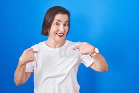 Foto de Middle age hispanic woman standing over blue background looking confident with smile on face, pointing oneself with fingers proud and happy. - Imagen libre de derechos