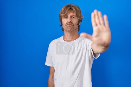 Photo for Middle age man standing over blue background doing stop sing with palm of the hand. warning expression with negative and serious gesture on the face. - Royalty Free Image