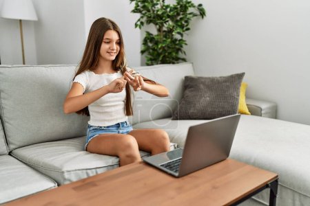 Téléchargez les photos : Adorable fille ayant un appel vidéo communiquant avec un langage sourd assis sur un canapé à la maison - en image libre de droit