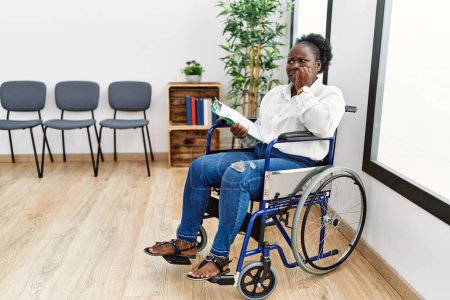 Téléchargez les photos : Jeune femme noire assise en fauteuil roulant dans la salle d'attente l'air stressée et nerveuse avec les mains sur les ongles mordants de la bouche. problème d'anxiété. - en image libre de droit