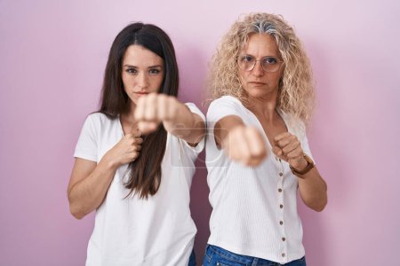 Téléchargez les photos : Mère et fille debout ensemble sur fond rose poing à coups de poing pour se battre, attaque agressive et en colère, menace et violence - en image libre de droit