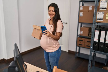Téléchargez les photos : Jeune femme latine travailleuse d'affaires enceinte utilisant un forfait de maintien de smartphone au bureau - en image libre de droit