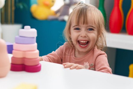 Foto de Adorable blonde girl playing with construction blocks sitting on table at kindergarten - Imagen libre de derechos