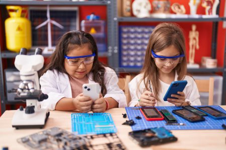 Foto de Dos niños estudiantes usando teléfonos inteligentes de pie en el aula de laboratorio - Imagen libre de derechos