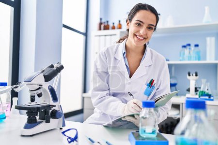 Téléchargez les photos : Jeune femme hispanique portant l'uniforme scientifique mesurant le liquide au laboratoire - en image libre de droit