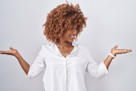 Téléchargez les photos : Jeune femme hispanique aux cheveux bouclés debout sur fond blanc souriant montrant les paumes ouvertes des deux mains, présentant et comparant la publicité et l'équilibre - en image libre de droit