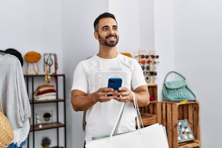 Foto de Joven cliente hispano usando compras de teléfonos inteligentes en la tienda de ropa - Imagen libre de derechos