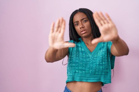 Téléchargez les photos : Young african american with braids standing over pink background doing frame using hands palms and fingers, camera perspective - en image libre de droit