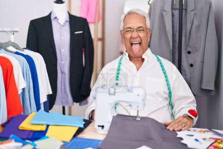 Photo for Middle age man with grey hair dressmaker using sewing machine sticking tongue out happy with funny expression. emotion concept. - Royalty Free Image