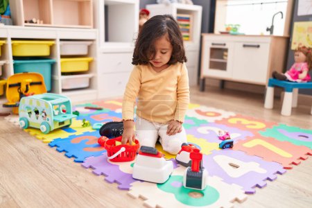 Photo for Adorable hispanic toddler playing with supermarket toy sitting on floor at kindergarten - Royalty Free Image