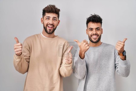 Photo for Young homosexual couple standing over white background success sign doing positive gesture with hand, thumbs up smiling and happy. cheerful expression and winner gesture. - Royalty Free Image