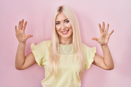 Téléchargez les photos : Femme blanche debout sur fond rose montrant et pointant vers le haut avec les doigts numéro dix tout en souriant confiant et heureux. - en image libre de droit