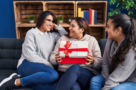 Photo for Three woman surprise with gift sitting on sofa at home - Royalty Free Image