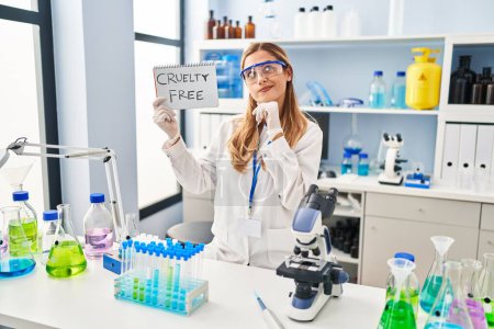Foto de Young blonde scientist woman working on cruelty free laboratory serious face thinking about question with hand on chin, thoughtful about confusing idea - Imagen libre de derechos