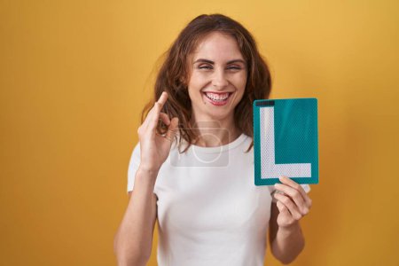 Photo for Beautiful brunette woman holding l sign for new driver doing ok sign with fingers, smiling friendly gesturing excellent symbol - Royalty Free Image
