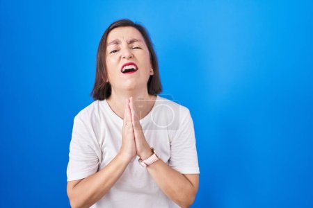 Photo for Middle age hispanic woman standing over blue background begging and praying with hands together with hope expression on face very emotional and worried. begging. - Royalty Free Image