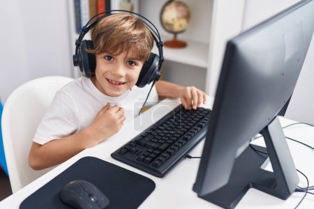 Téléchargez les photos : Adorable étudiant garçon caucasien utilisant l'ordinateur assis sur la table en classe - en image libre de droit