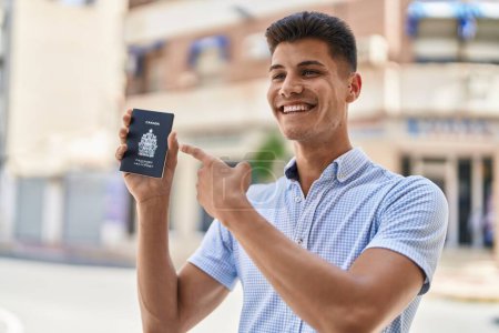 Photo for Young hispanic man smiling confident pointing to canada passport at street - Royalty Free Image