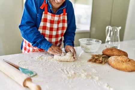 Téléchargez les photos : Senior homme souriant confiant keading pâte avec les mains à la cuisine - en image libre de droit