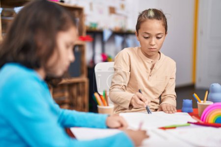 Foto de Dos niños estudiantes sentados en mesa dibujo sobre papel en el jardín de infantes - Imagen libre de derechos