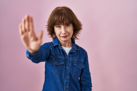 Photo for Middle age woman standing over pink background doing stop sing with palm of the hand. warning expression with negative and serious gesture on the face. - Royalty Free Image