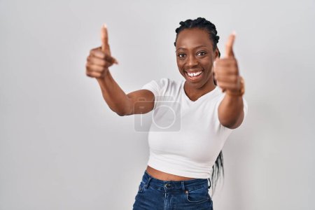 Foto de Beautiful black woman standing over isolated background approving doing positive gesture with hand, thumbs up smiling and happy for success. winner gesture. - Imagen libre de derechos