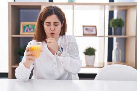 Téléchargez les photos : Brunette woman drinking glass of orange juice feeling unwell and coughing as symptom for cold or bronchitis. health care concept. - en image libre de droit