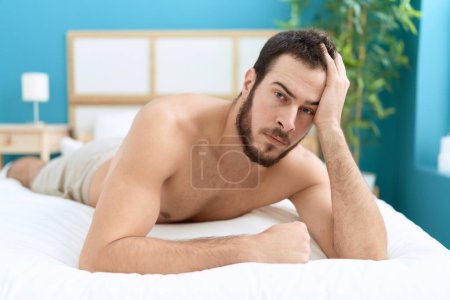 Téléchargez les photos : Young hispanic man lying on bed with relaxed expression at bedroom - en image libre de droit