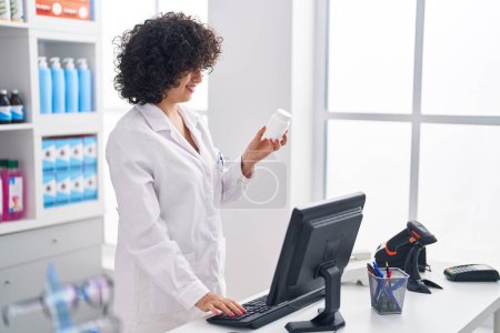 Téléchargez les photos : Young middle east woman pharmacist using computer holding pills at pharmacy - en image libre de droit