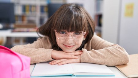Photo for Adorable hispanic girl student sitting on table leaning on book at classroom - Royalty Free Image