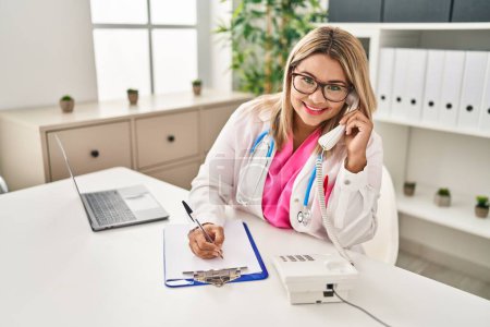 Téléchargez les photos : Jeune femme hispanique portant l'uniforme de médecin parlant au téléphone travail al clinique - en image libre de droit