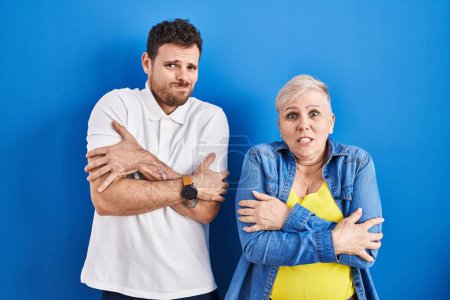 Foto de Young brazilian mother and son standing over blue background shaking and freezing for winter cold with sad and shock expression on face - Imagen libre de derechos