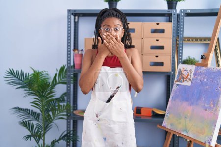 Photo for Young african american with braids at art studio painting on canvas shocked covering mouth with hands for mistake. secret concept. - Royalty Free Image