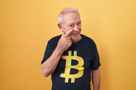 Photo for Senior man with grey hair wearing bitcoin t shirt pointing to the eye watching you gesture, suspicious expression - Royalty Free Image