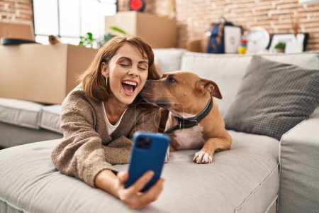 Photo for Young caucasian woman make selfie by the smartphone lying on sofa with dog at new home - Royalty Free Image